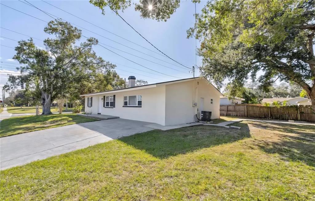 A single-story house with a concrete driveway, white exterior walls, and large surrounding oak trees — 1004 N BETTY LANE, CLEARWATER, FL