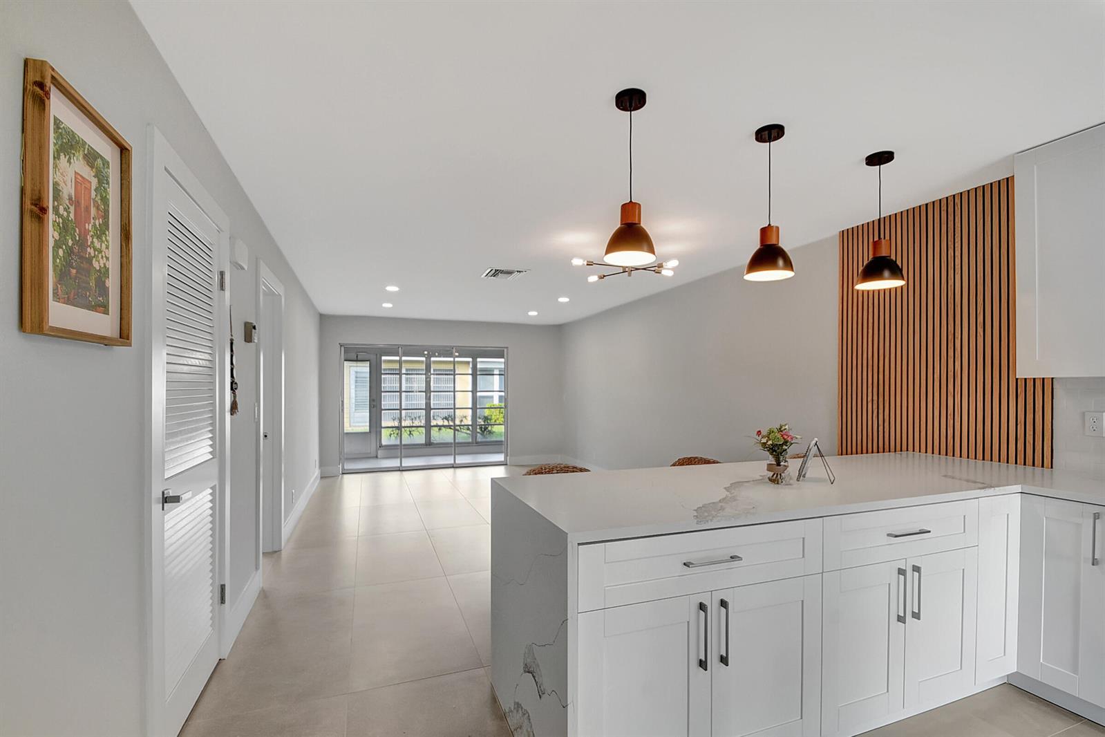 A kitchen features a white island with three woven bar stools and wood-slat wall paneling — 13602 Via Flora Apt C, Delray Beach FL 33484, DELRAY BEACH, FL