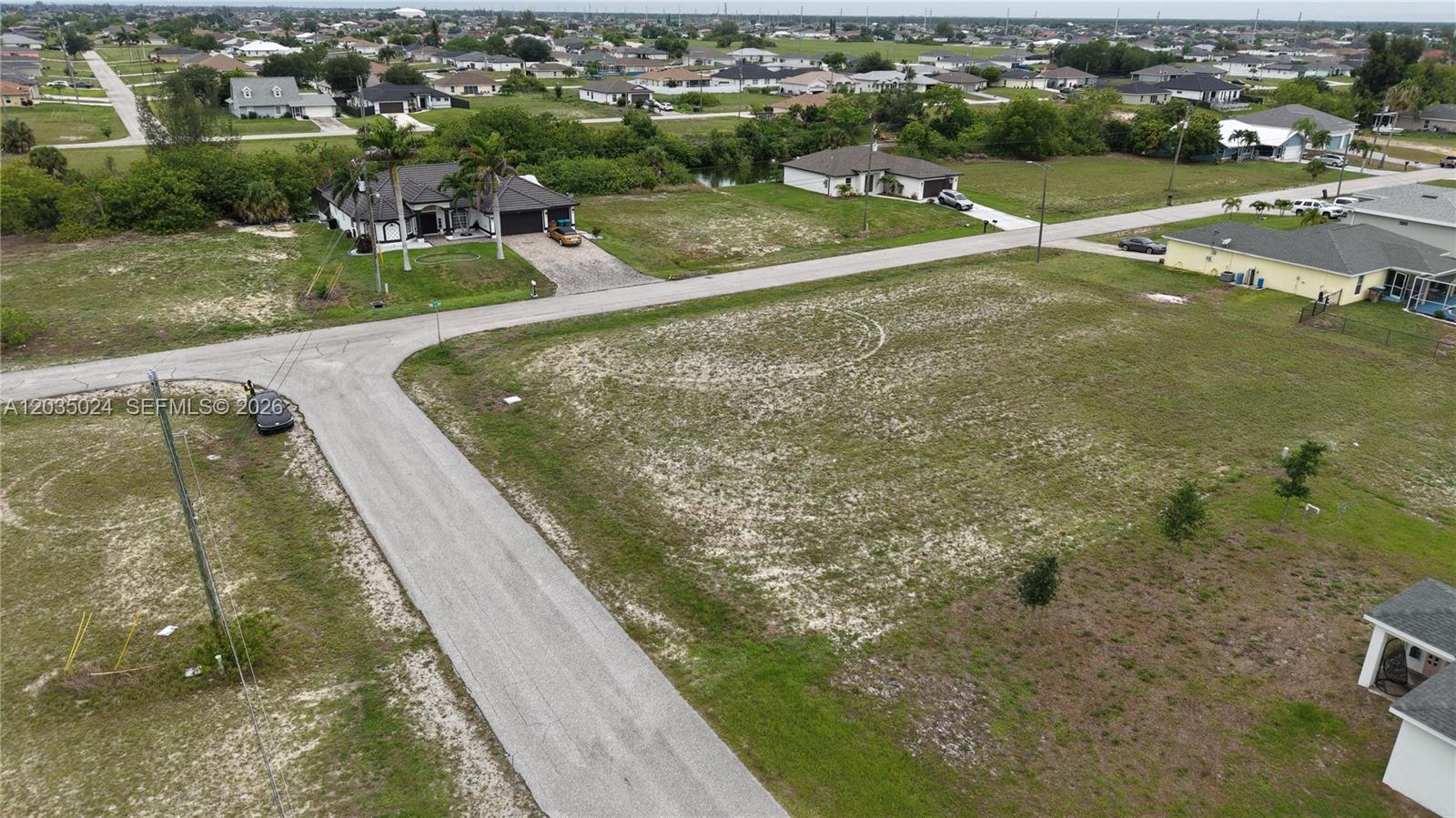 An aerial view shows a vacant corner lot next to a house with palm trees — 2009 NW 2ND AVE, Cape Coral FL 33993, CAPE CORAL, FL