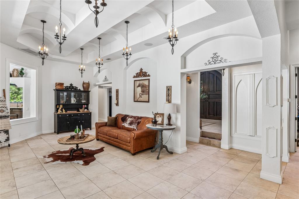 A spacious living room features vaulted ceilings, tile flooring, a leather sofa, and multiple chandeliers — 3530 OLD KEYSTONE ROAD, TARPON SPRINGS, FL