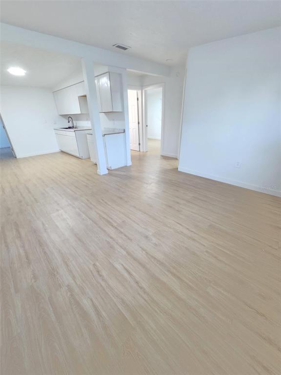 An open-concept living area features light wood-look flooring and a white kitchen with white cabinets — 6703 SANDRA DRIVE, PORT RICHEY, FL