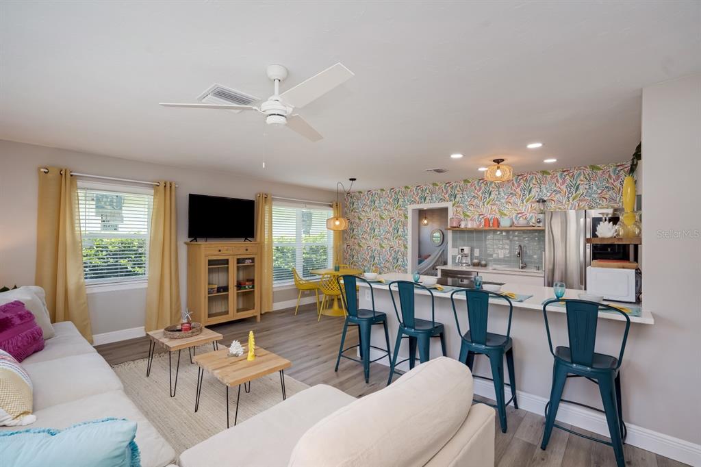 An open-concept living room and kitchen feature floral wallpaper, teal bar stools, and wood flooring — 617 26TH STREET W, BRADENTON, FL