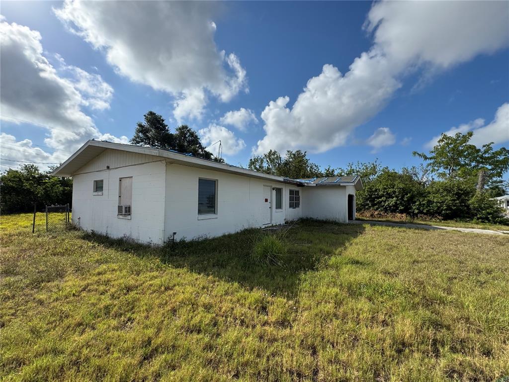A white, single-story concrete block house stands in a grassy lot under a cloudy sky — 325 TIMBRUCE LANE NW, PORT CHARLOTTE, FL