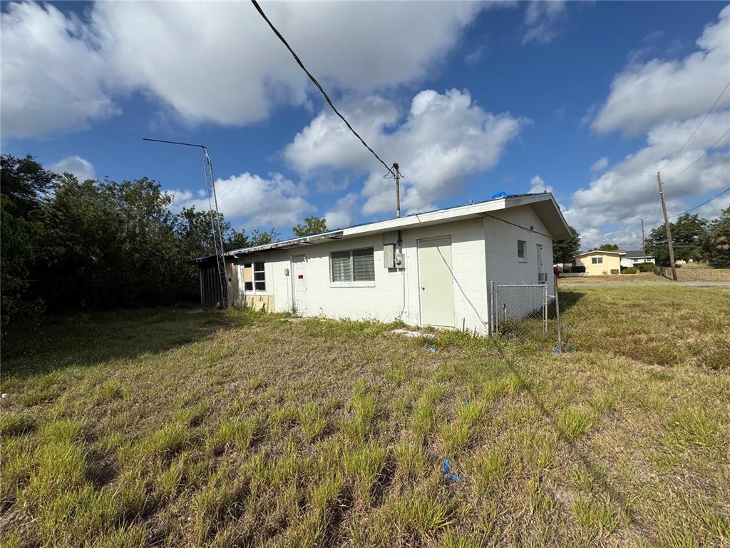 A single-story white concrete block building sits on a grassy lot under a cloudy sky — 325 TIMBRUCE LANE NW, PORT CHARLOTTE, FL