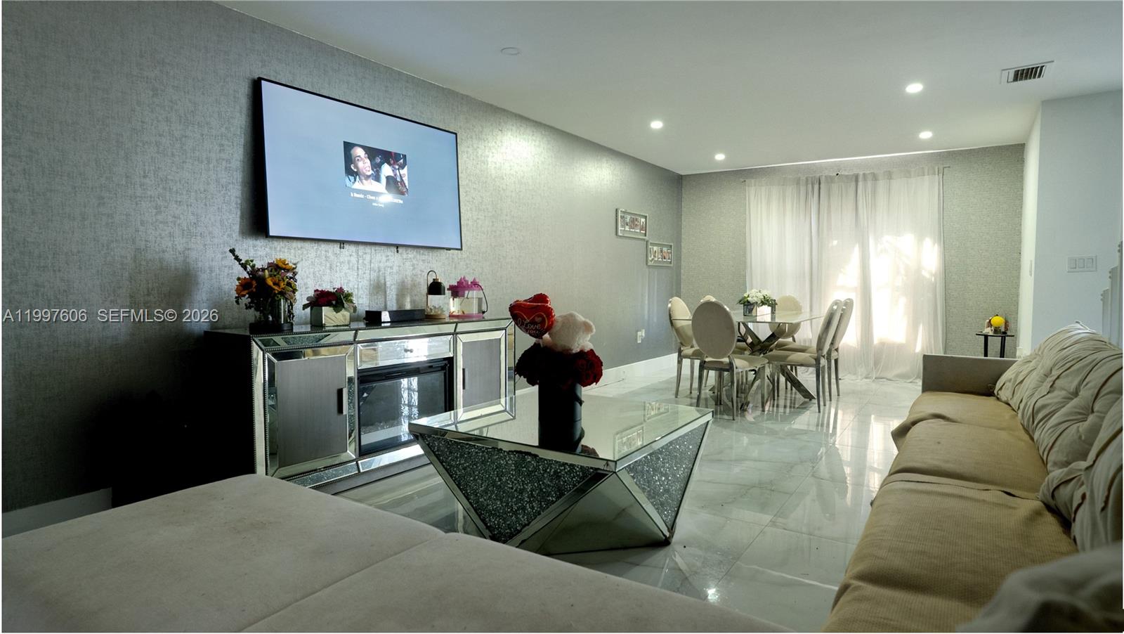 A living and dining area features a mirrored coffee table, fireplace console, and tiled floors — 18499 NW 52nd Path, Miami Gardens FL 33055, MIAMI GARDENS, FL