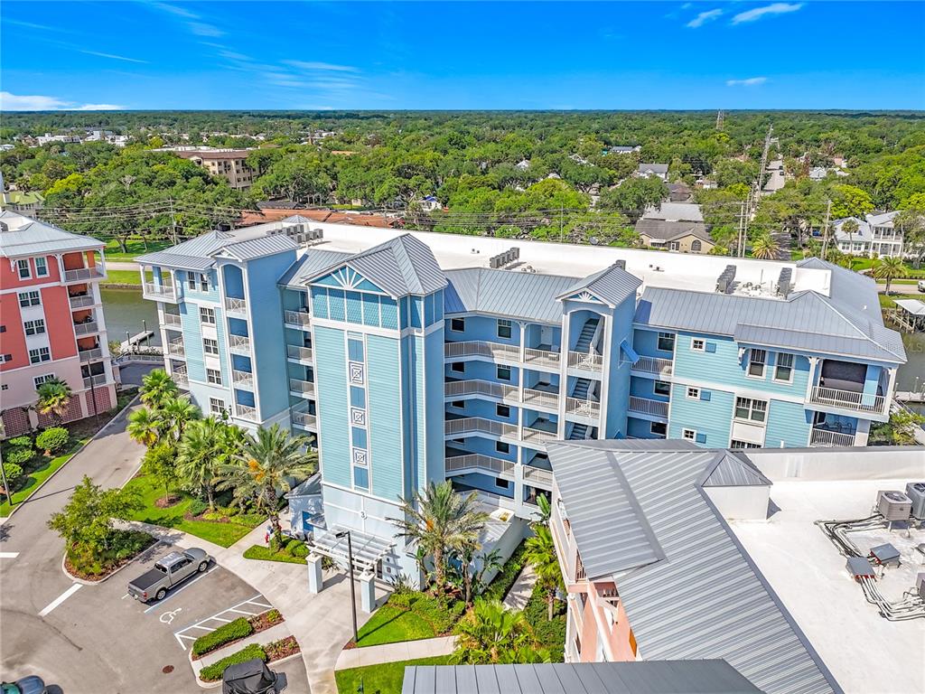 An aerial view shows a multi-story blue residential building with a metal roof and parking — 3 RIVERWALK DRIVE UNIT 301, NEW SMYRNA BEACH, FL