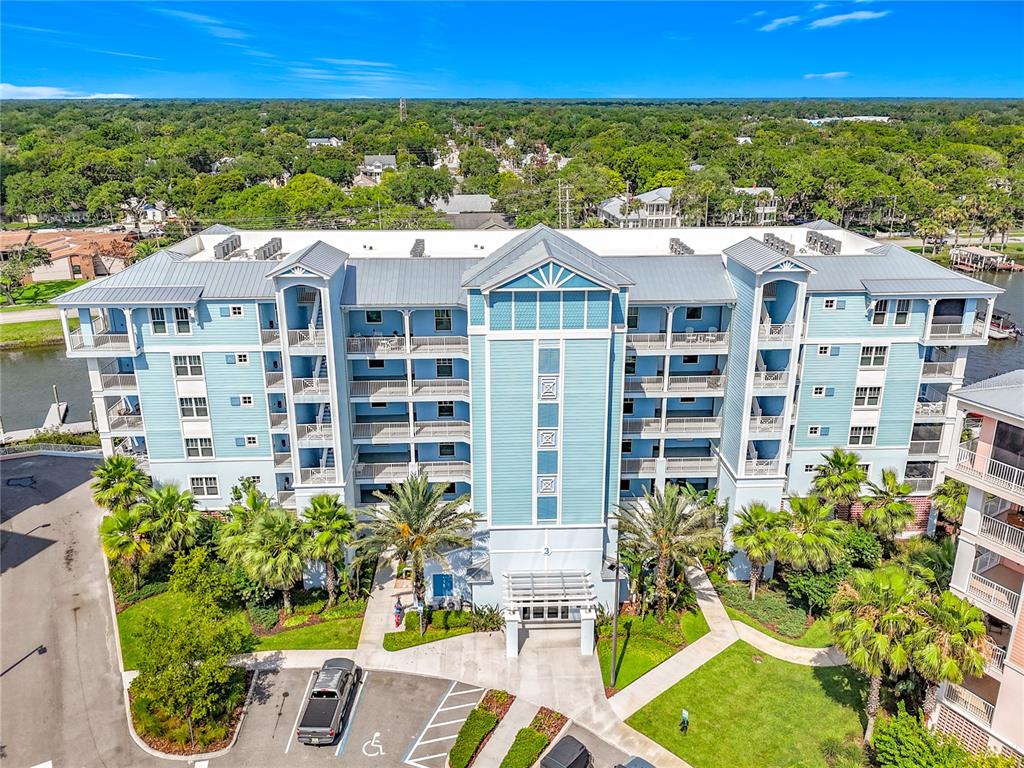 An aerial view of a multi-story blue apartment building with balconies and surrounding palm trees — 3 RIVERWALK DRIVE UNIT 301, NEW SMYRNA BEACH, FL