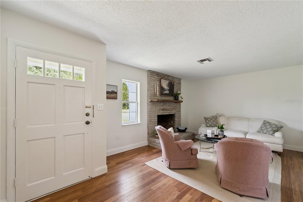 A living room features a brick fireplace, hardwood floors, two pink armchairs, and a sofa — 2650 HARRY AVENUE, ORANGE CITY, FL