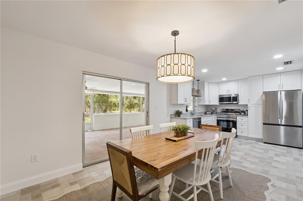 A dining area with a wooden table and white chairs sits adjacent to a modern kitchen — 2650 HARRY AVENUE, ORANGE CITY, FL