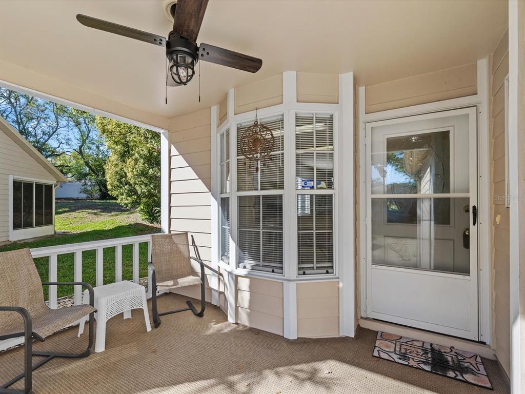 A covered porch features a ceiling fan, two chairs, a bay window, and a front door — 4505 GLEN HOLLOW, NEW PORT RICHEY, FL