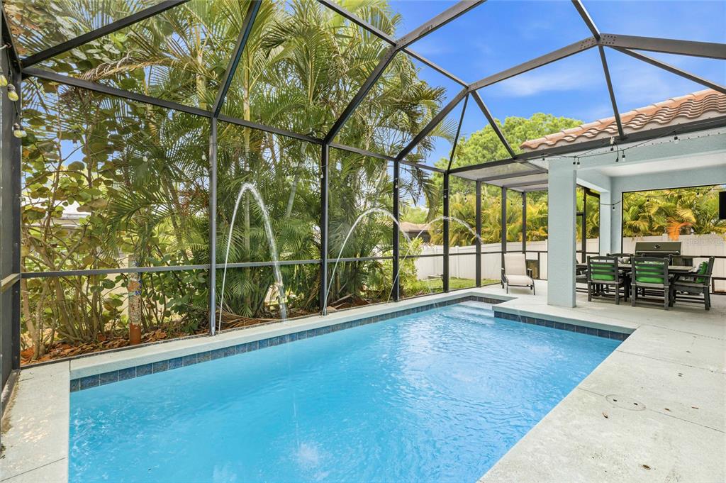A screened-in swimming pool with water fountains sits on a patio next to outdoor furniture — 5603 AARON COURT, SARASOTA, FL