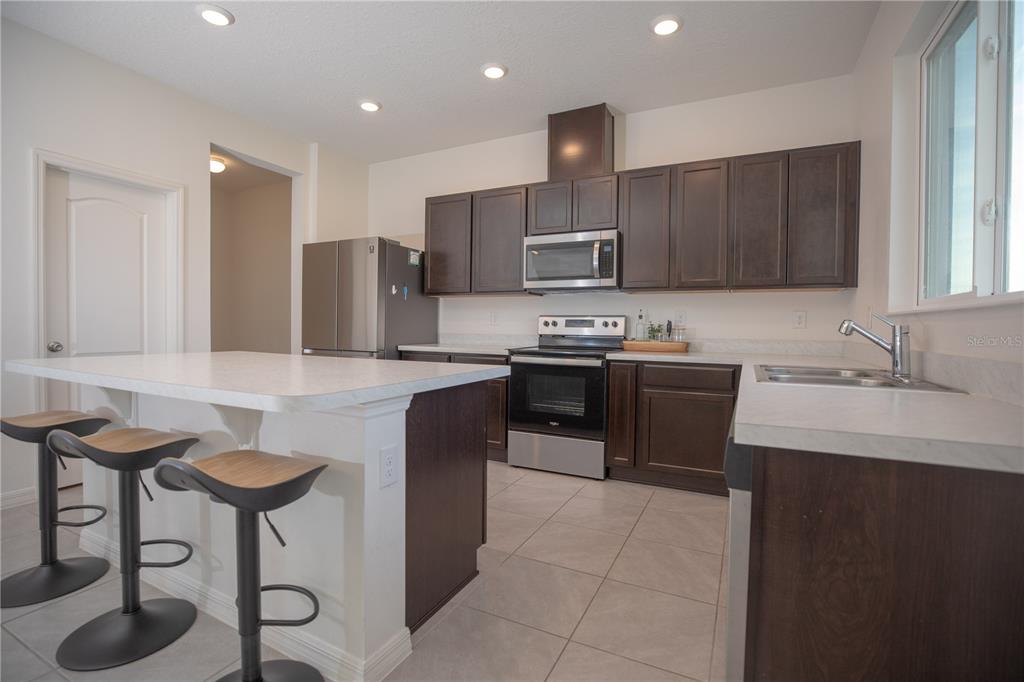 A kitchen features dark wood cabinets, stainless steel appliances, a white island, and tile flooring — 1531 FUJI COURT, WINTER HAVEN, FL