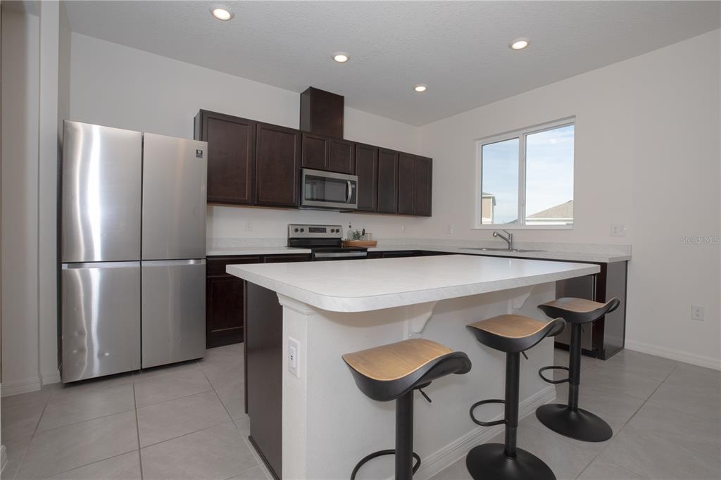 A kitchen features dark wood cabinets, stainless steel appliances, a white island, and tile flooring — 1531 FUJI COURT, WINTER HAVEN, FL