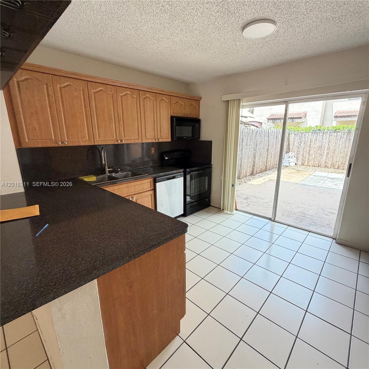 A kitchen features wood cabinets, dark countertops, white tile floors, and a sliding glass door — 680 NW 82nd Pl # 264, Miami FL 33126, MIAMI, FL