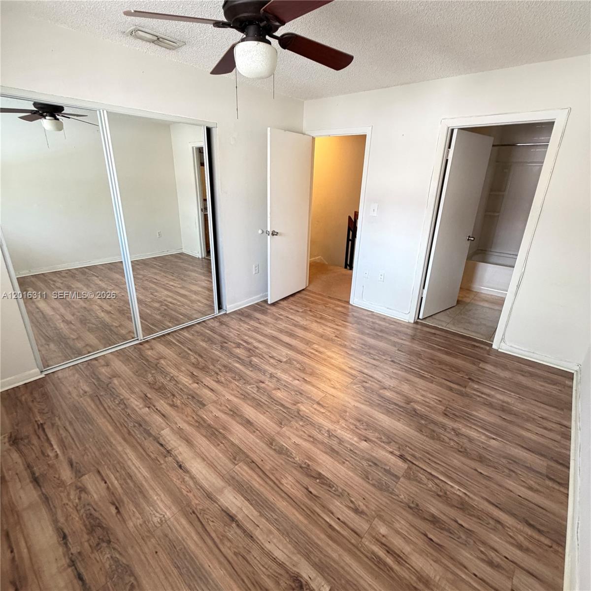 A bedroom features wood-look flooring, mirrored closet doors, a ceiling fan, and two doorways — 680 NW 82nd Pl # 264, Miami FL 33126, MIAMI, FL