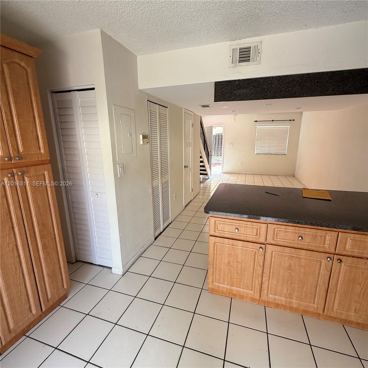 A kitchen with light wood cabinets and dark countertops overlooks a tiled living area — 680 NW 82nd Pl # 264, Miami FL 33126, MIAMI, FL