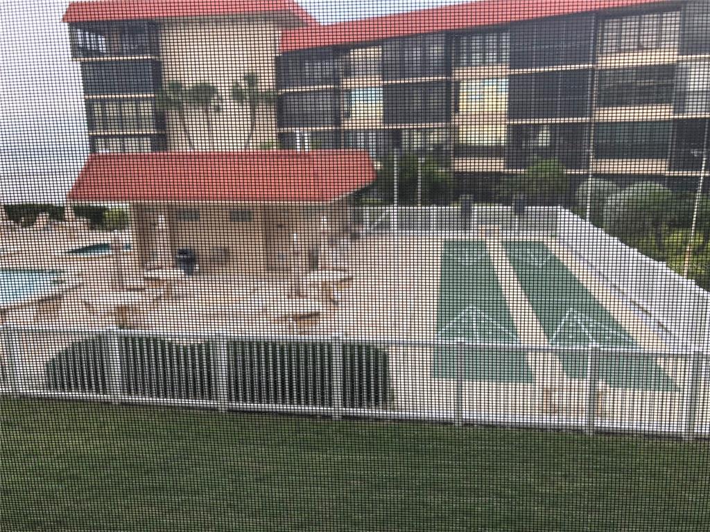 A view through a screen shows a swimming pool area with shuffleboard courts and buildings — 17580 GULF BOULEVARD UNIT 206, REDINGTON SHORES, FL