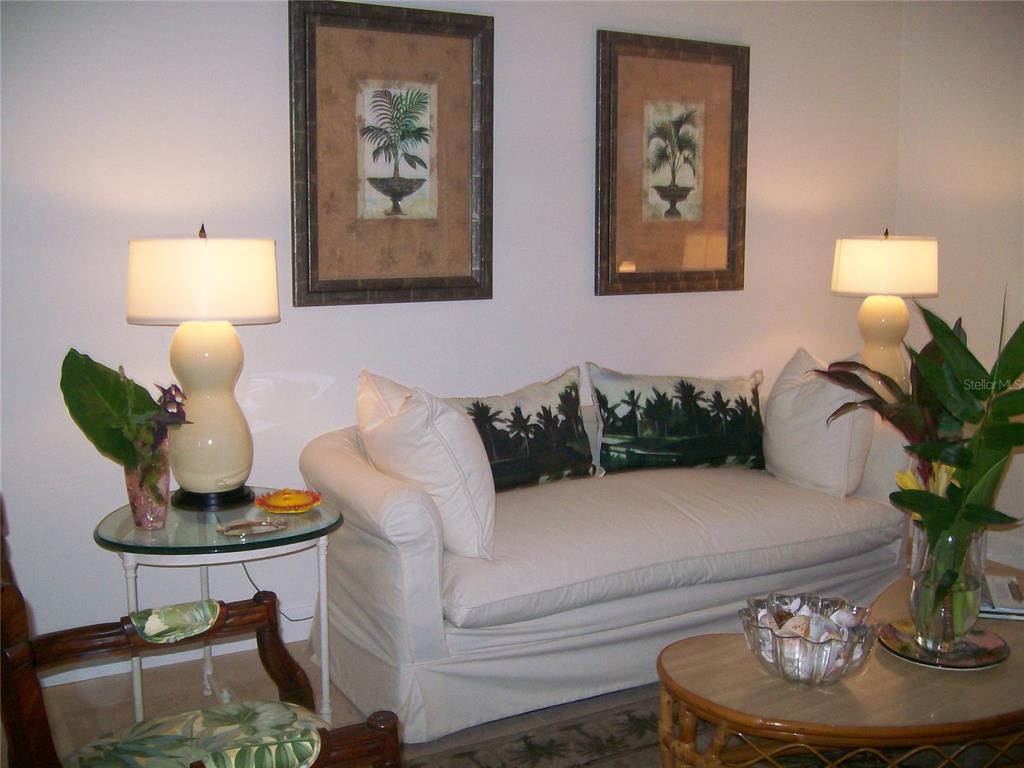 A living room features a white sofa, two lamps, and tropical-themed wall art — 17580 GULF BOULEVARD UNIT 206, REDINGTON SHORES, FL