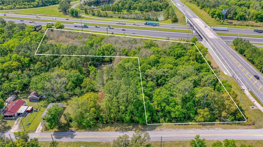 An aerial view shows a wooded lot outlined in white next to a highway overpass — W MAIN STREET, LAKE HELEN, FL