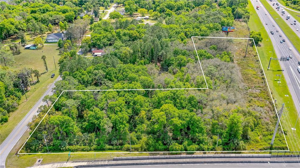 An aerial view shows a wooded, L-shaped plot of land bordered by a highway and road — W MAIN STREET, LAKE HELEN, FL