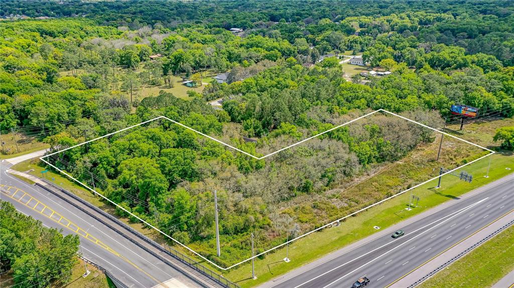 An aerial view shows a vacant, wooded lot outlined in white next to a highway — W MAIN STREET, LAKE HELEN, FL