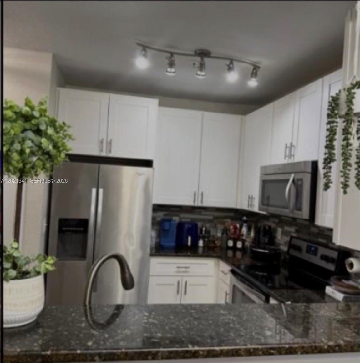 A kitchen features white cabinets, stainless steel appliances, dark countertops, and a curved track light — 204 E South street # 1061, Orlando FL 32801, ORLANDO, FL