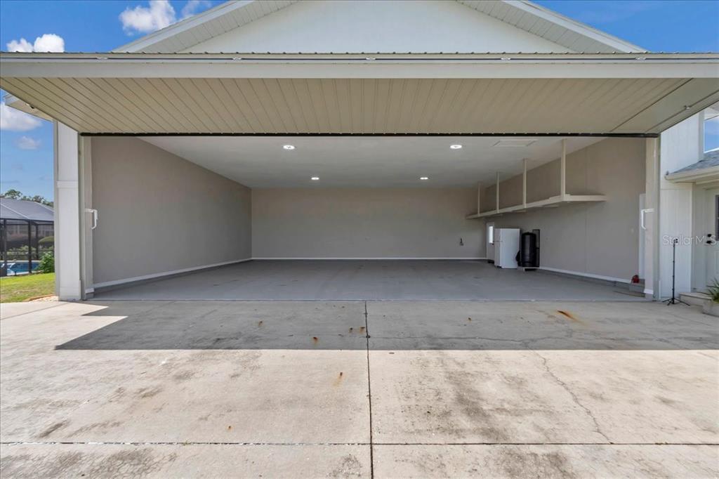 A wide-open garage with a large overhead door, concrete flooring, and recessed ceiling lighting — 9700 SE 72ND AVENUE, OCALA, FL