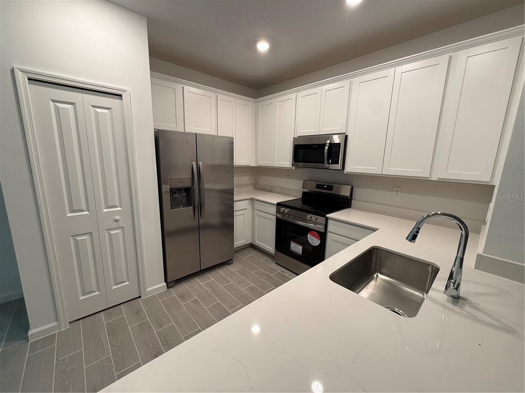 A modern kitchen features white cabinets, stainless steel appliances, and light-colored quartz countertops — 3674 SE 37TH COURT, OCALA, FL