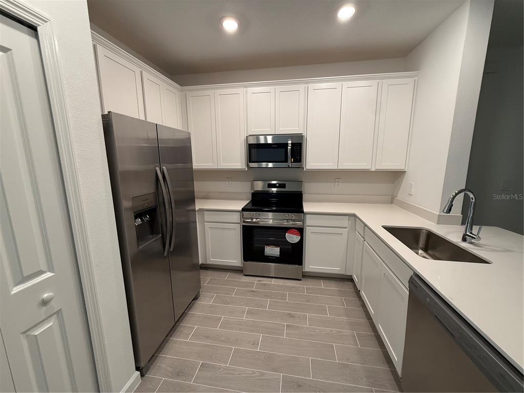 A kitchen features white cabinets, stainless steel appliances, light countertops, and gray tile flooring — 3674 SE 37TH COURT, OCALA, FL