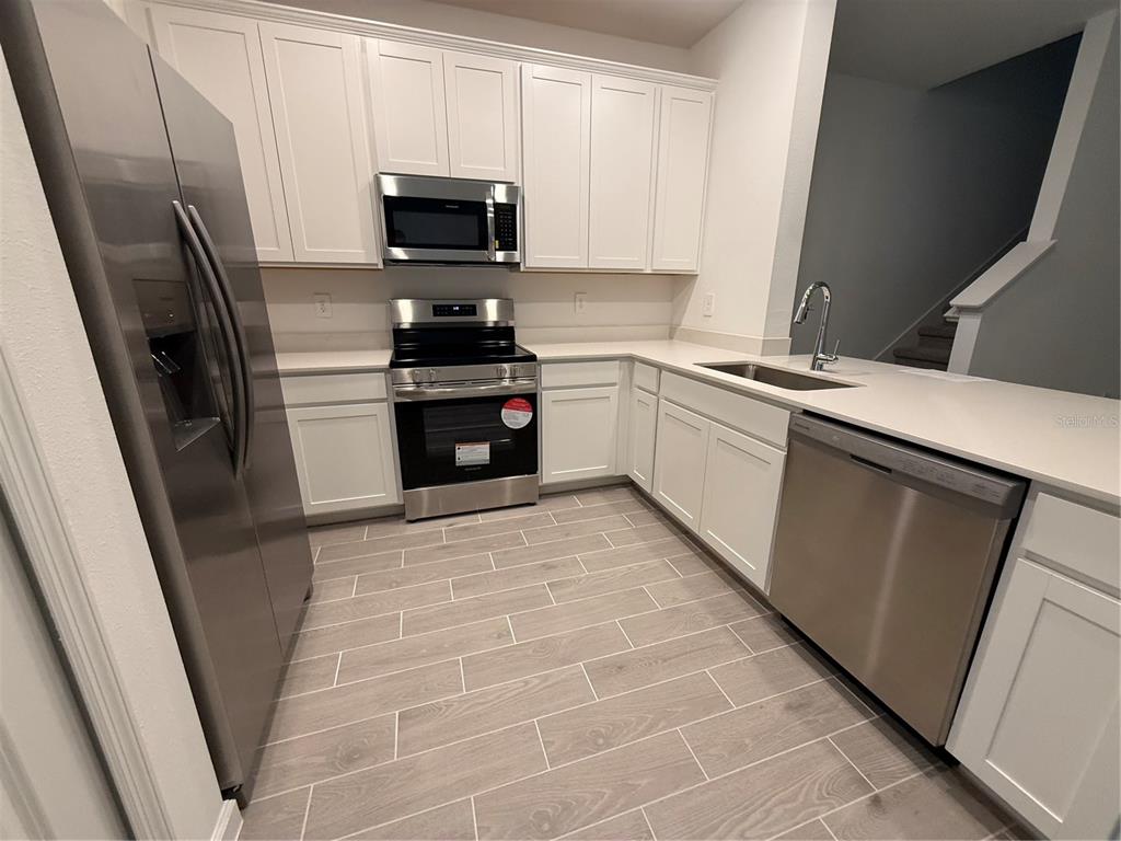A kitchen features white cabinets, stainless steel appliances, light countertops, and wood-look tile flooring — 3674 SE 37TH COURT, OCALA, FL