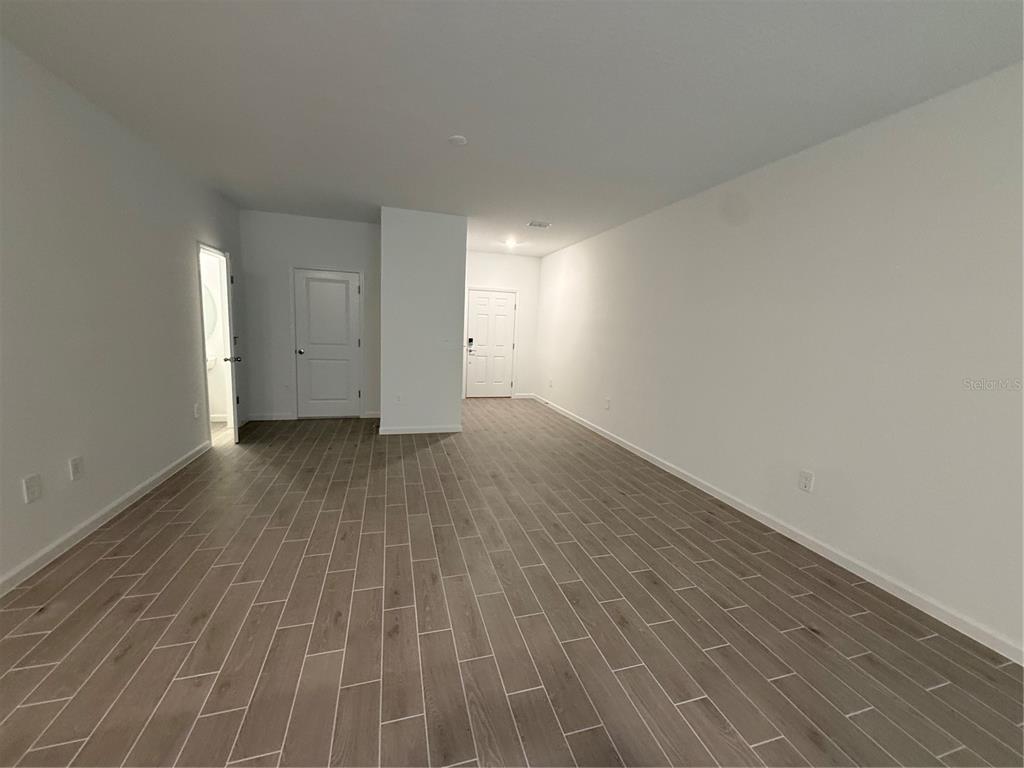 An empty room with white walls, wood-look tile flooring, and three interior doors — 3674 SE 37TH COURT, OCALA, FL