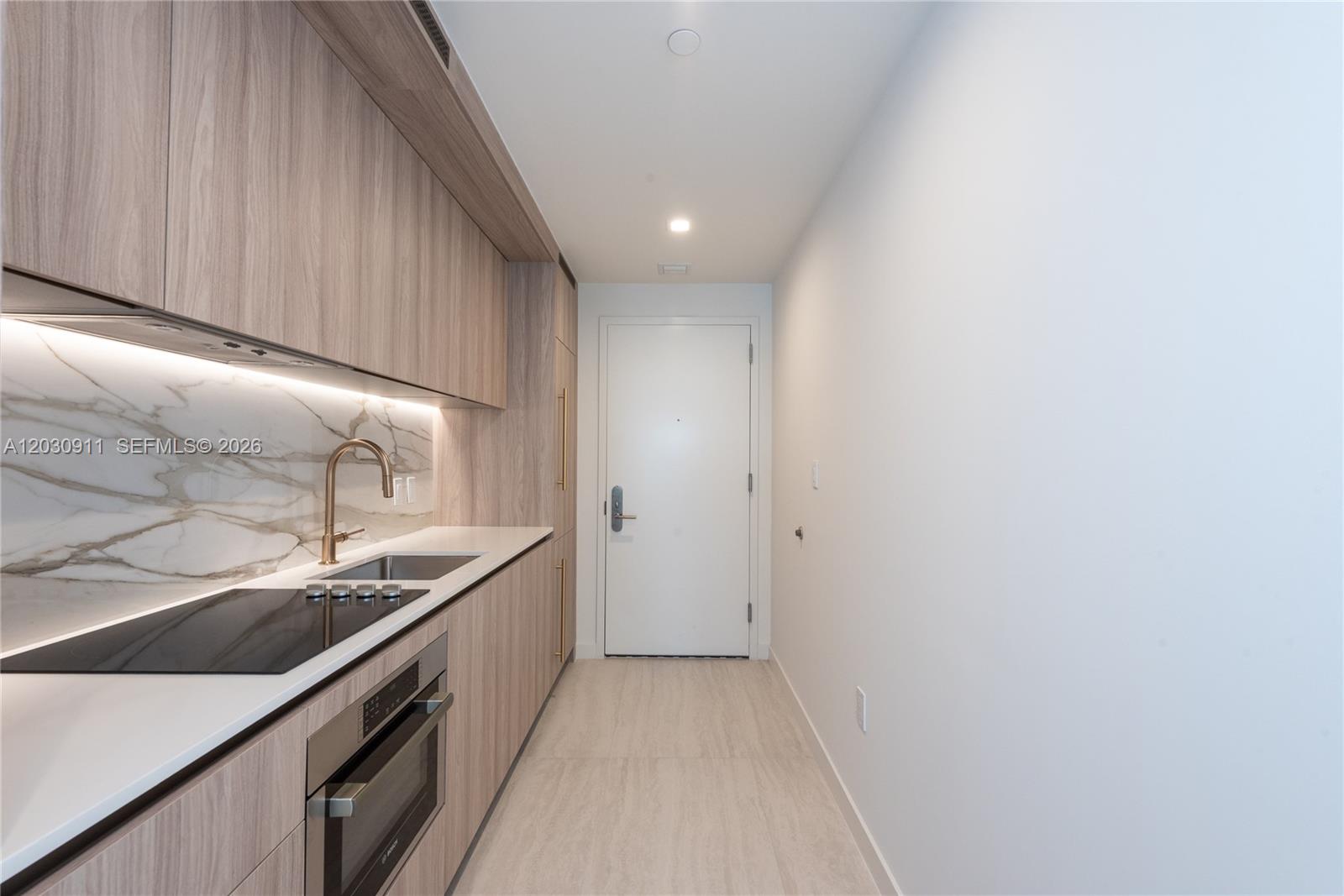 A modern galley kitchen features light wood cabinetry, white countertops, and a marble backsplash — 77 SE 5th Street # 1804, Miami FL 33131, MIAMI, FL