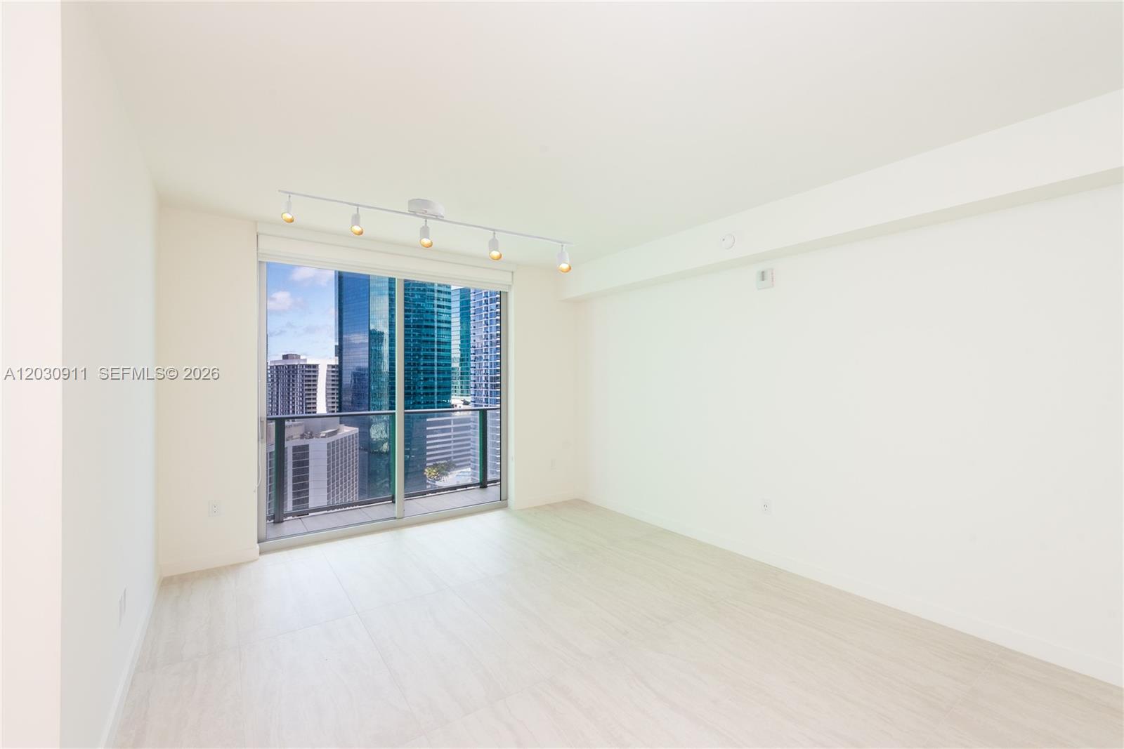 An empty room features light-colored flooring, white walls, track lighting, and a balcony with city views — 77 SE 5th Street # 1804, Miami FL 33131, MIAMI, FL