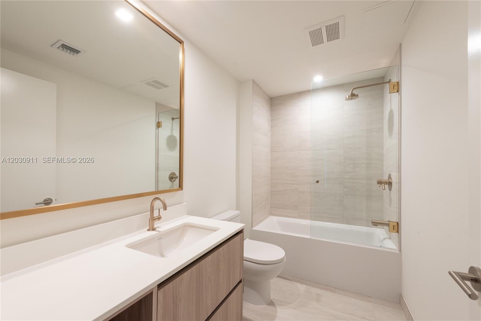 A modern bathroom features a wood vanity, a gold-framed mirror, and a glass-enclosed tub shower — 77 SE 5th Street # 1804, Miami FL 33131, MIAMI, FL