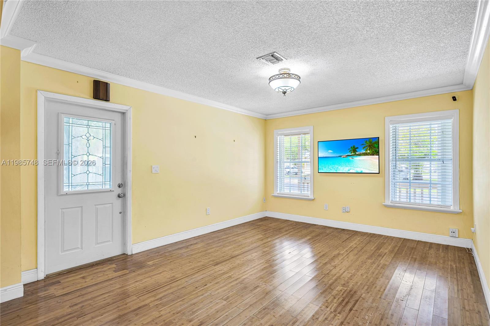 A living room with yellow walls, wood flooring, a ceiling light, and a wall-mounted television — 11455 SW 117 Ct, Miami FL 33186, MIAMI, FL
