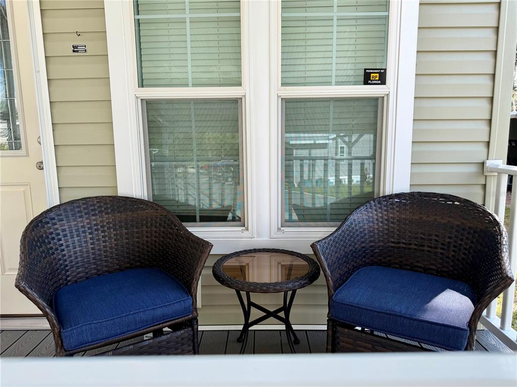 Two wicker chairs with blue cushions and a small glass table sit on a porch — 699 CINDI AVENUE, LEESBURG, FL