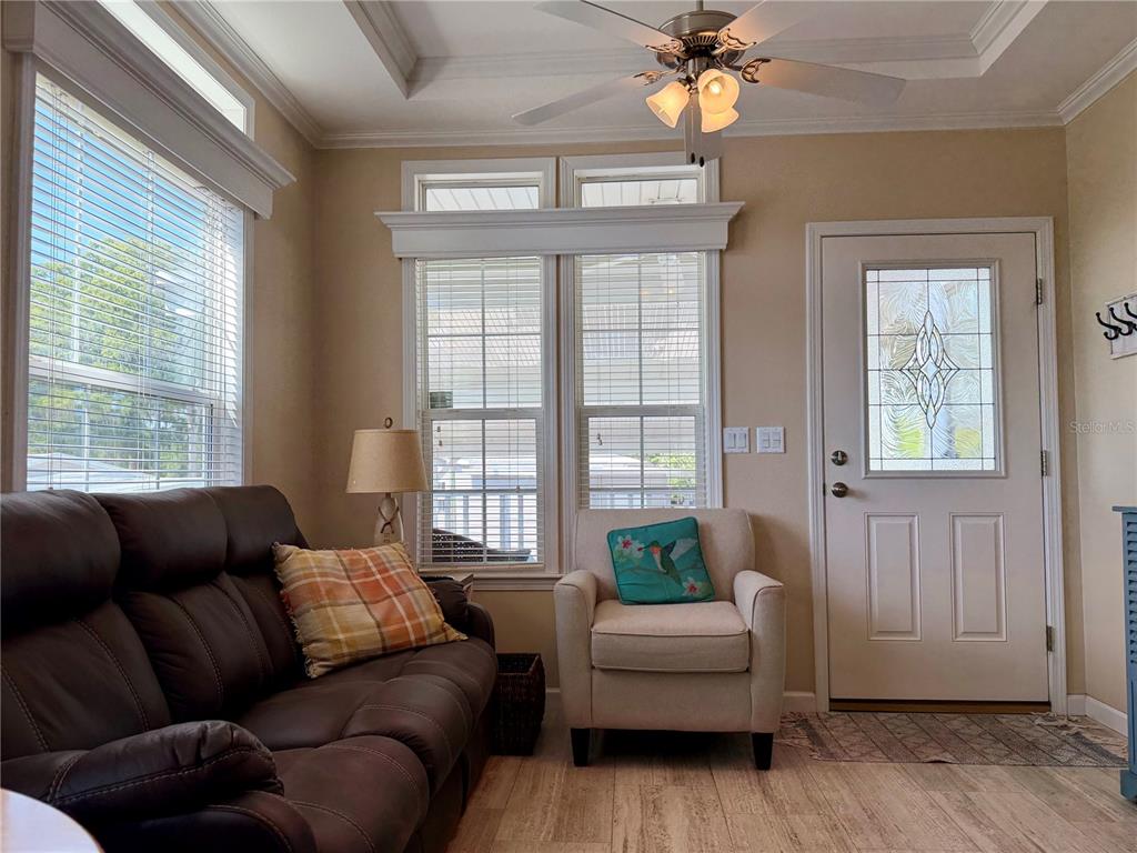 A living room features a brown sofa, an armchair, windows with blinds, and a ceiling fan — 699 CINDI AVENUE, LEESBURG, FL