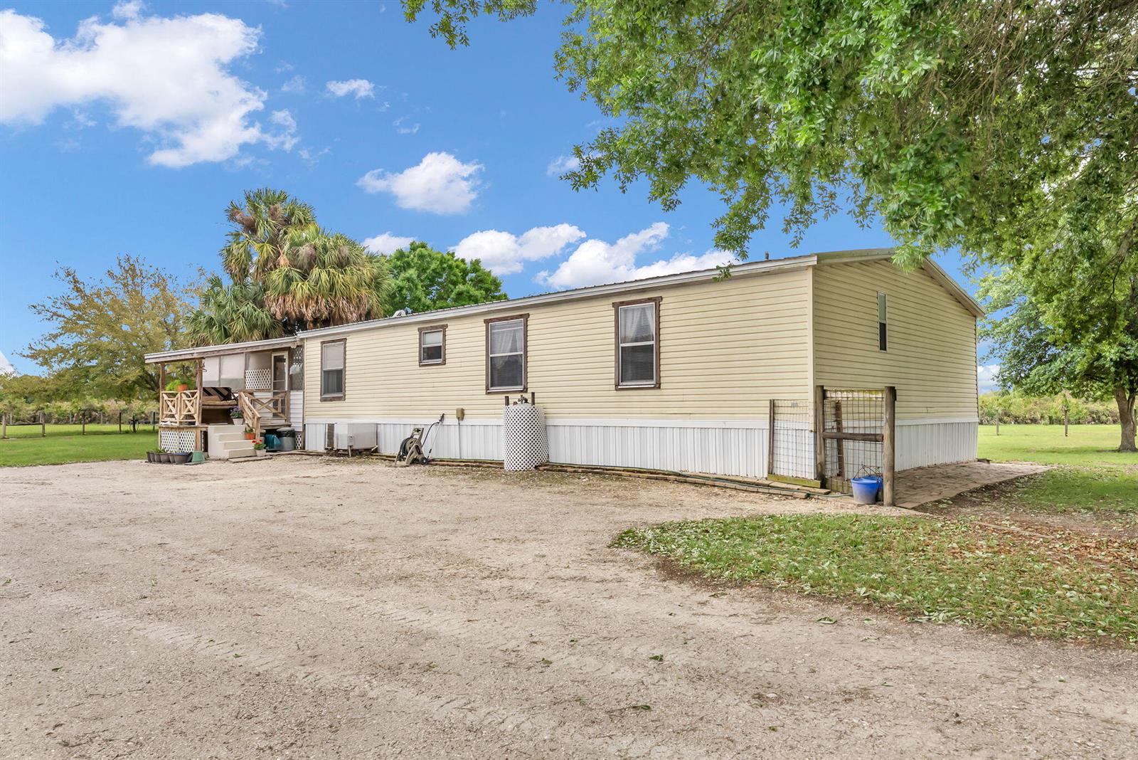 A single-story manufactured home with light yellow siding sits on a gravel lot — 17255 NW 272nd Street, Okeechobee FL 34972, OKEECHOBEE, FL