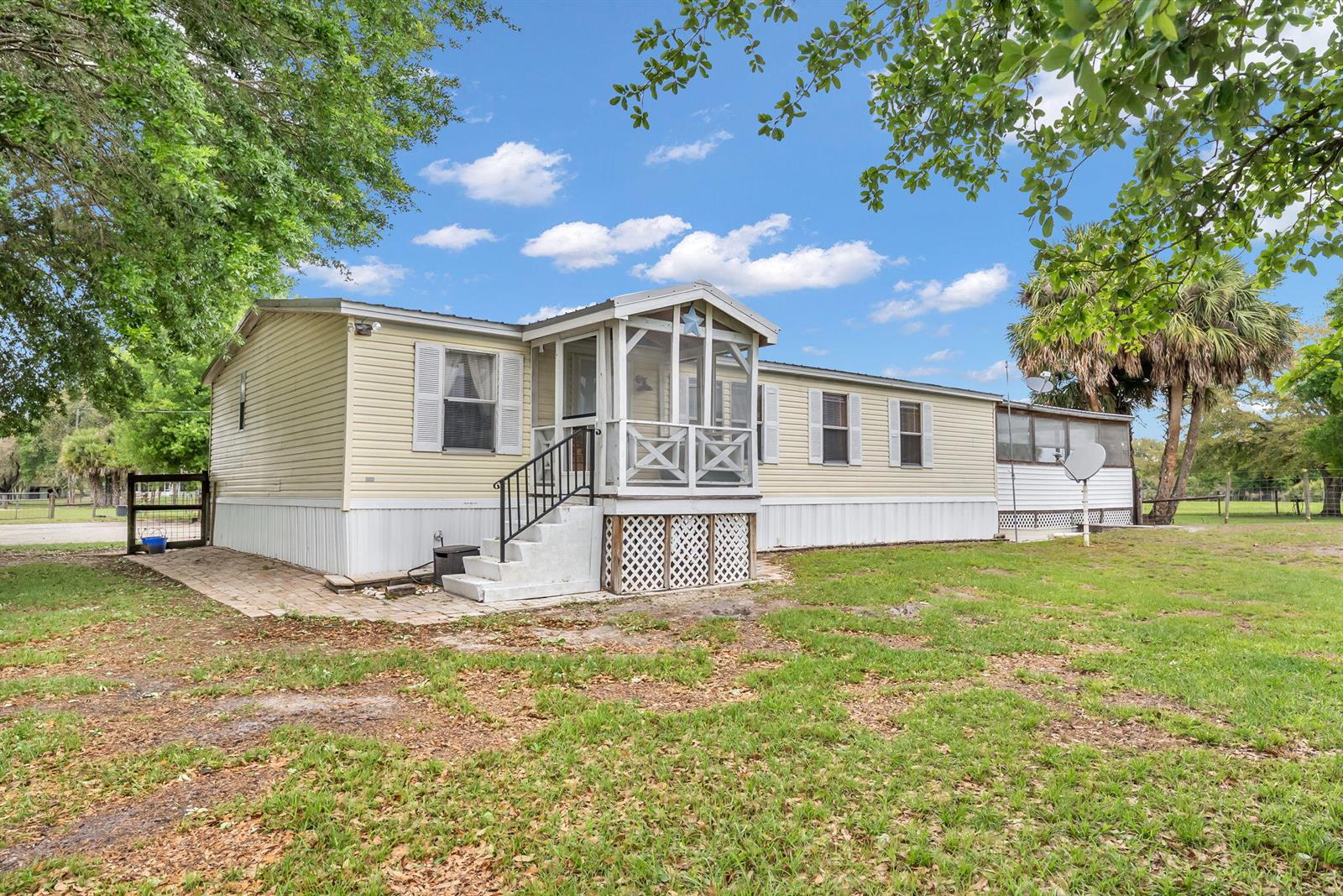 A light yellow manufactured home features a screened-in front porch and white lattice skirting — 17255 NW 272nd Street, Okeechobee FL 34972, OKEECHOBEE, FL