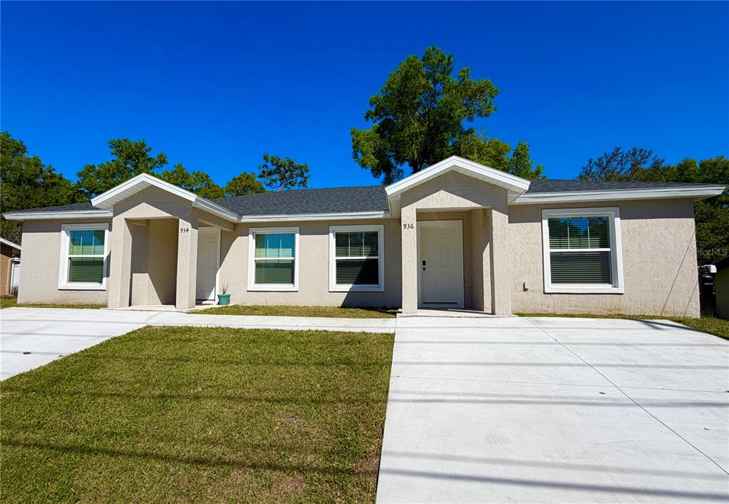 A single-story duplex with a beige exterior, two front entrances, and a concrete driveway — 934 S APOPKA AVENUE, INVERNESS, FL