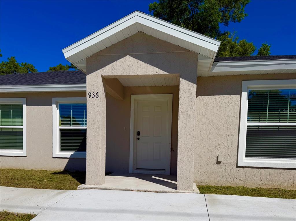 The exterior of a single-story house features a covered entryway, a white door, and windows — 934 S APOPKA AVENUE, INVERNESS, FL