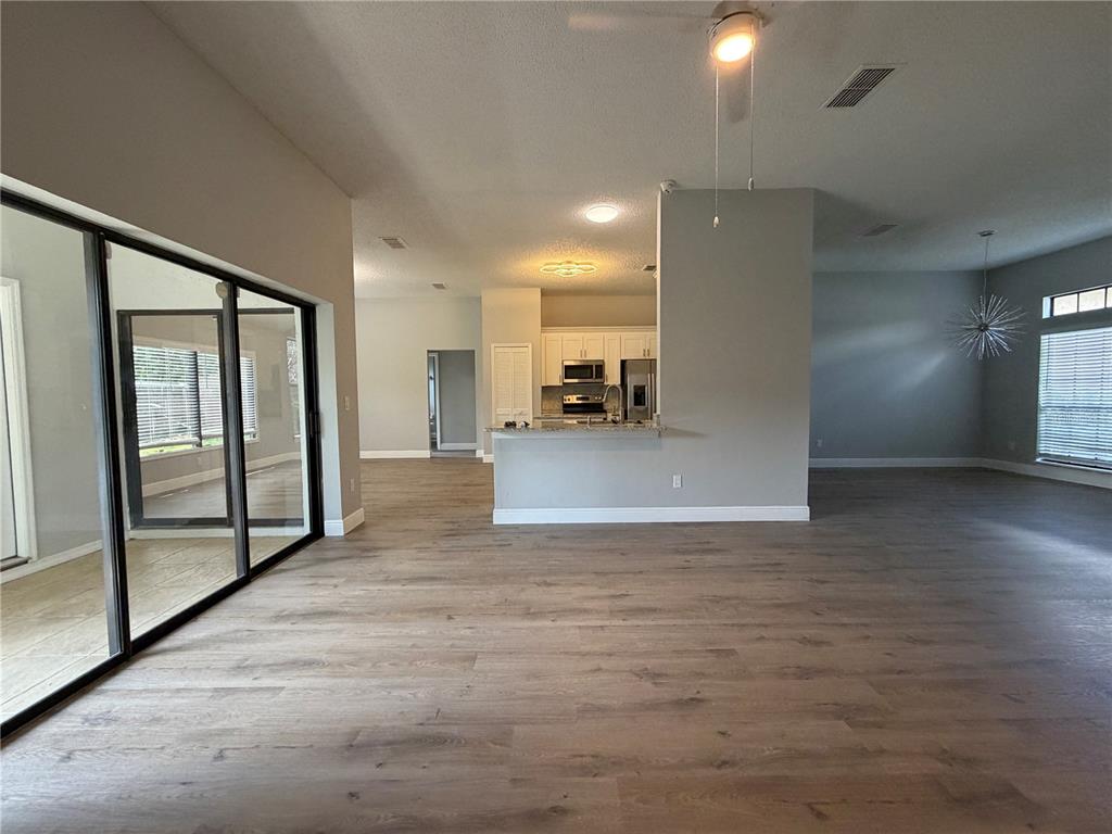 An open-concept living area features light wood-look flooring, a central kitchen, and sliding glass doors — 1009 CORKWOOD DRIVE, OVIEDO, FL