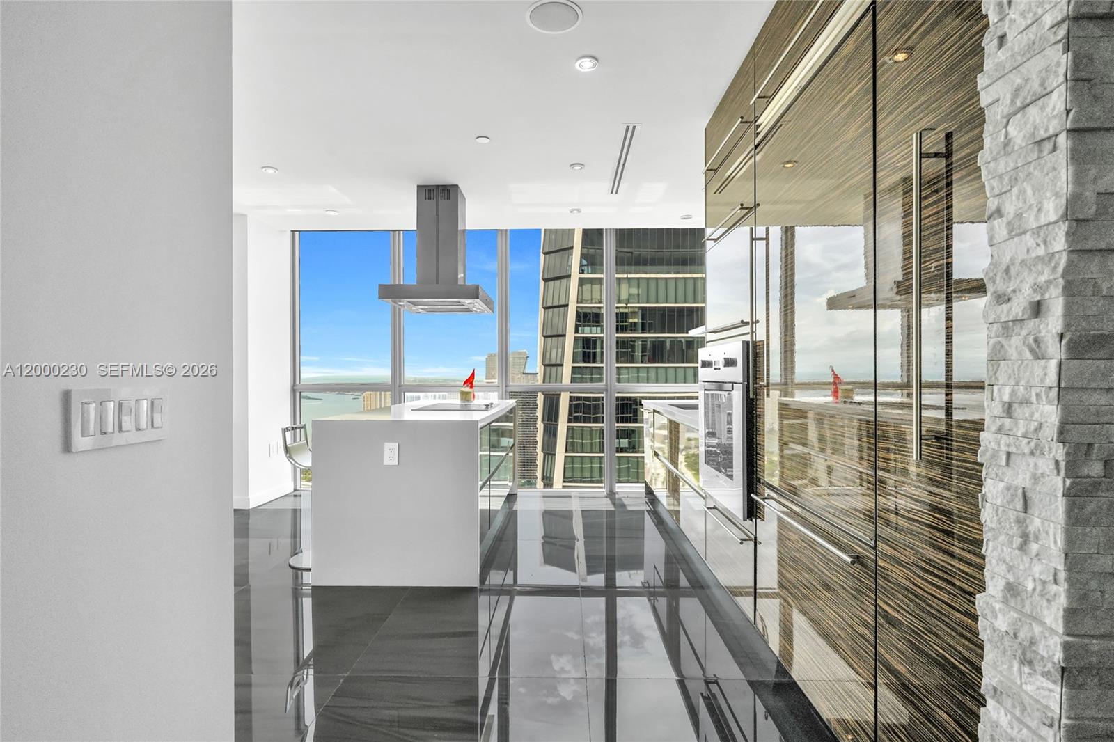 A modern kitchen features dark wood cabinetry, a white island, and floor-to-ceiling windows — 1100 Biscayne Blvd # 6001, Miami FL 33132, MIAMI, FL