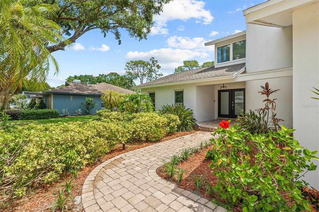 A paved walkway leads to the front entrance of a white house with a shingled roof — 13915 WHISPERWOOD DRIVE, CLEARWATER, FL