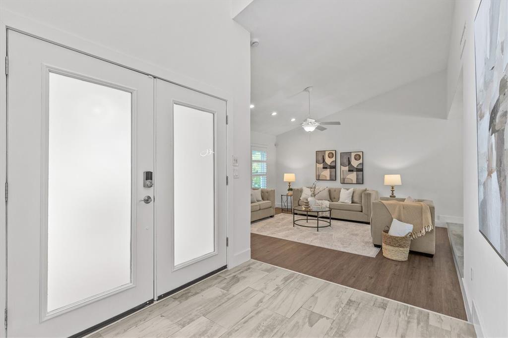 A bright entryway with tile flooring leads into a living room with wood-look floors — 13915 WHISPERWOOD DRIVE, CLEARWATER, FL
