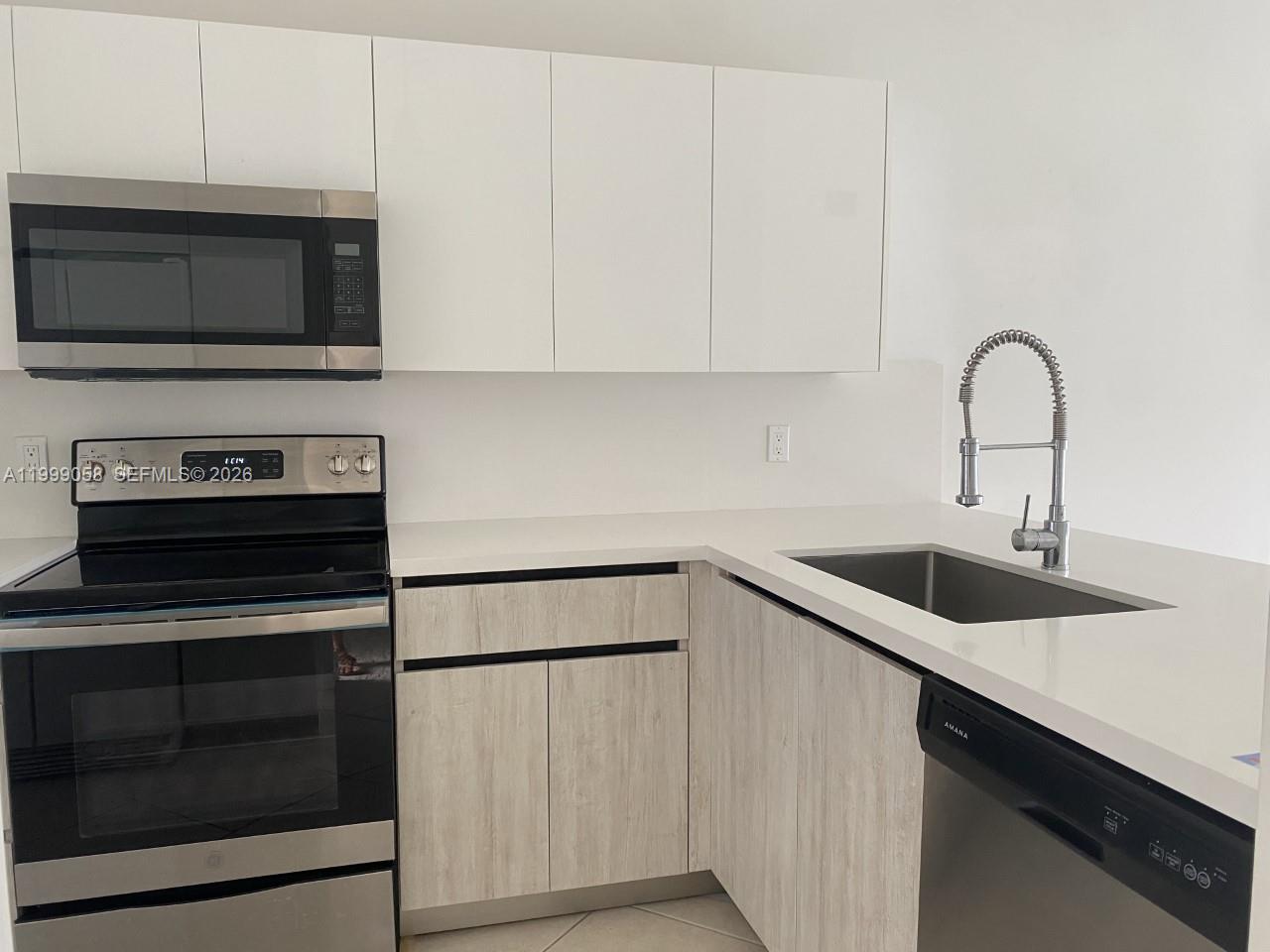 A modern kitchen features white upper cabinets, light wood-grain lower cabinets, and stainless steel appliances — 219 SE 8th St # 601, Hallandale Beach FL 33009, HALLANDALE BEACH, FL