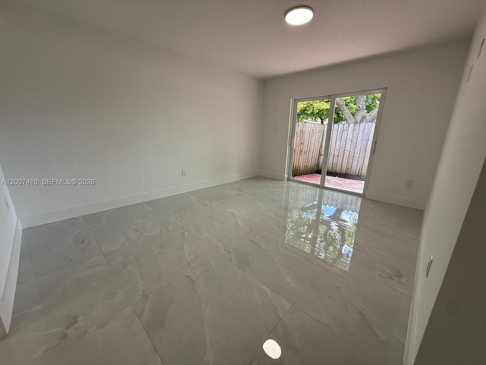 An empty room features large light-colored tile flooring and a sliding glass door to a patio — 10058 SW 156th Ct, Miami FL 33196, MIAMI, FL