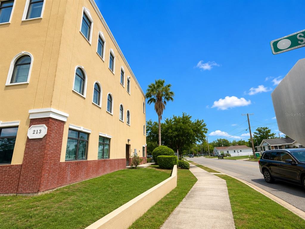 A three-story yellow building with brick accents stands beside a sidewalk and a street — 213 S DILLARD STREET UNIT 230, WINTER GARDEN, FL
