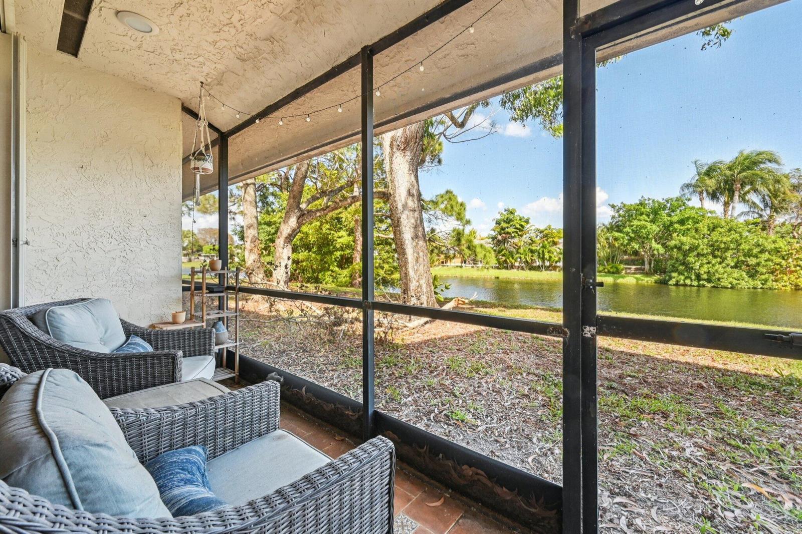 A screened-in patio features wicker chairs overlooking a grassy yard and a small pond — 22 Via De Casas # 103, Boynton Beach FL 33426, BOYNTON BEACH, FL