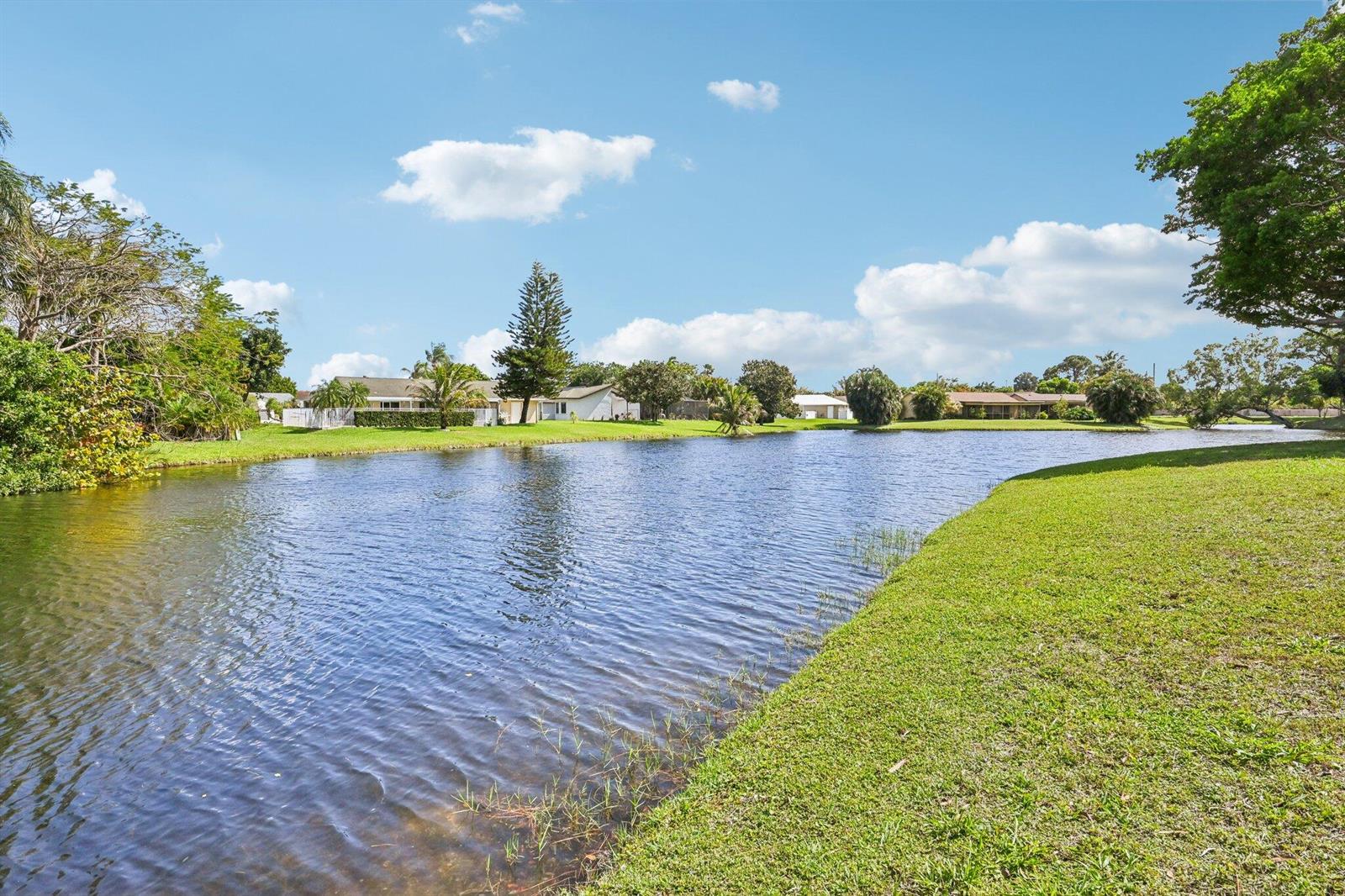A view of a calm lake surrounded by green lawns and residential houses — 22 Via De Casas # 103, Boynton Beach FL 33426, BOYNTON BEACH, FL